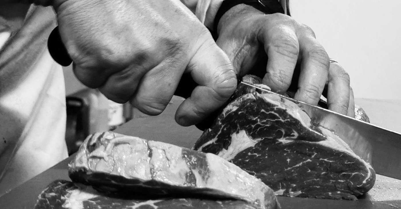 A butcher's hands trimming a cut of meat with a knife
